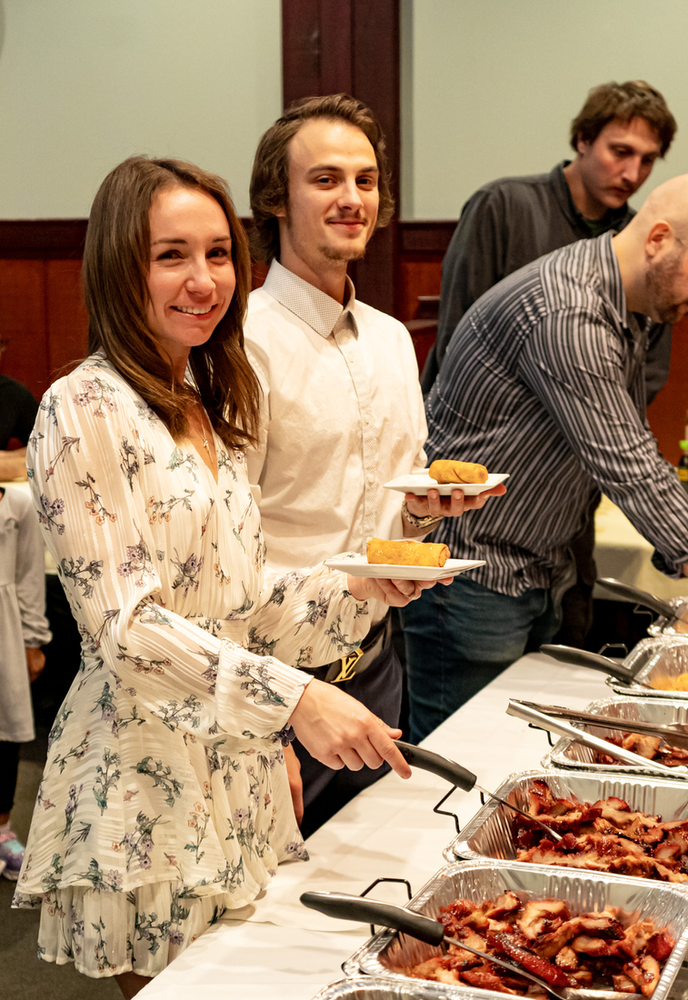 A man and a woman are standing at a buffet table holding plates of food.