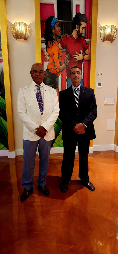 Two men in suits and ties are standing next to each other in front of a painting.