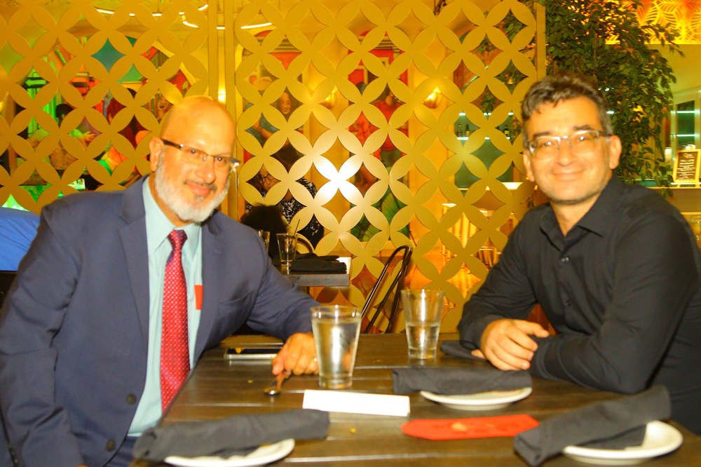 Two men sit at a table with plates and glasses