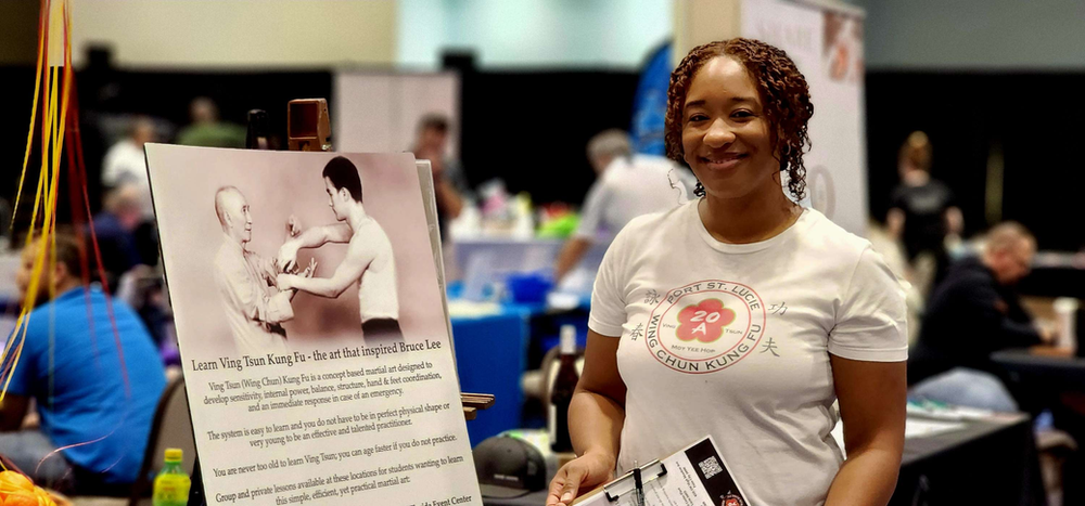 A woman is standing in front of a sign at a convention.