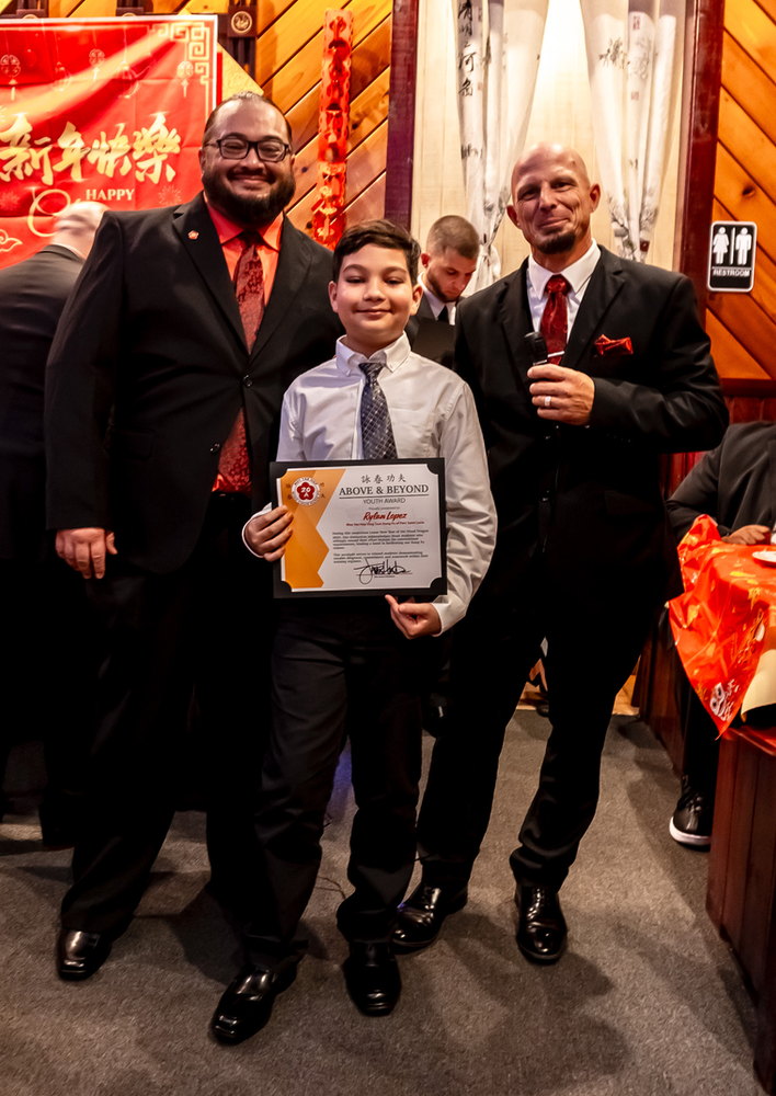 Three men are posing for a picture with a boy holding a certificate.