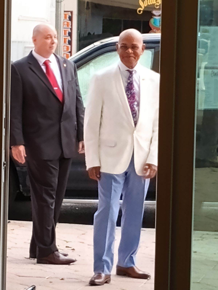 Two men in suits and ties are walking in front of a tattoo shop