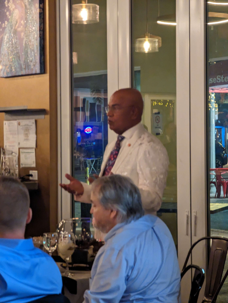 A man in a white shirt and tie is talking to a group of people