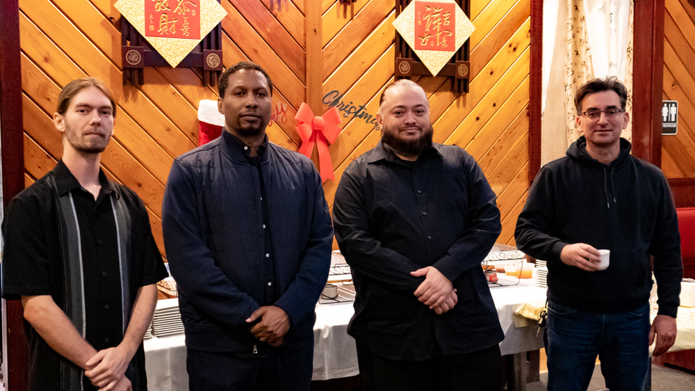 A group of men are standing next to each other in front of a wooden wall.