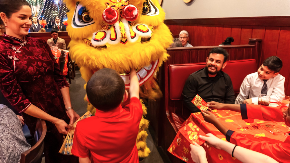 A group of people are sitting at a table in front of a lion costume.