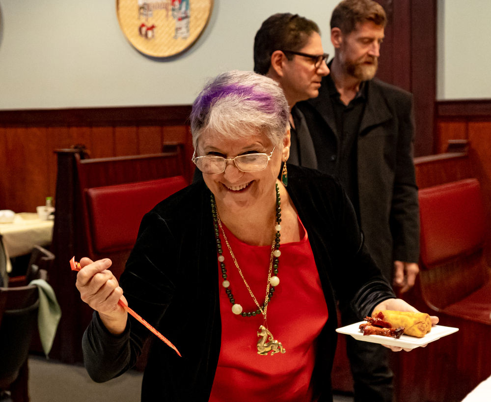 A woman with purple hair is smiling while holding a plate of food