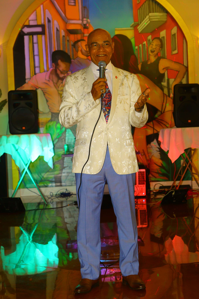 A man in a white jacket and blue pants is singing into a microphone