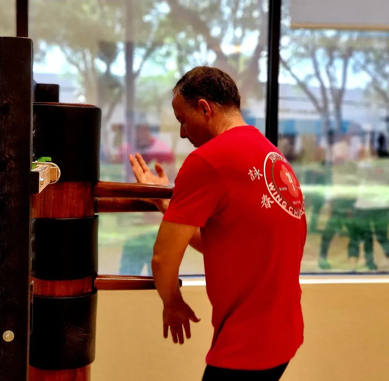 A man in a red shirt is standing next to a wooden dummy