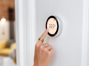 Person's finger touching a smart thermostat displaying 22 degrees Celsius, mounted on a white wall.