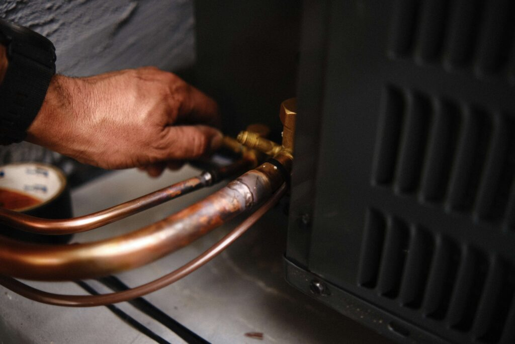 A person's hand connecting copper tubes to an air conditioning unit.