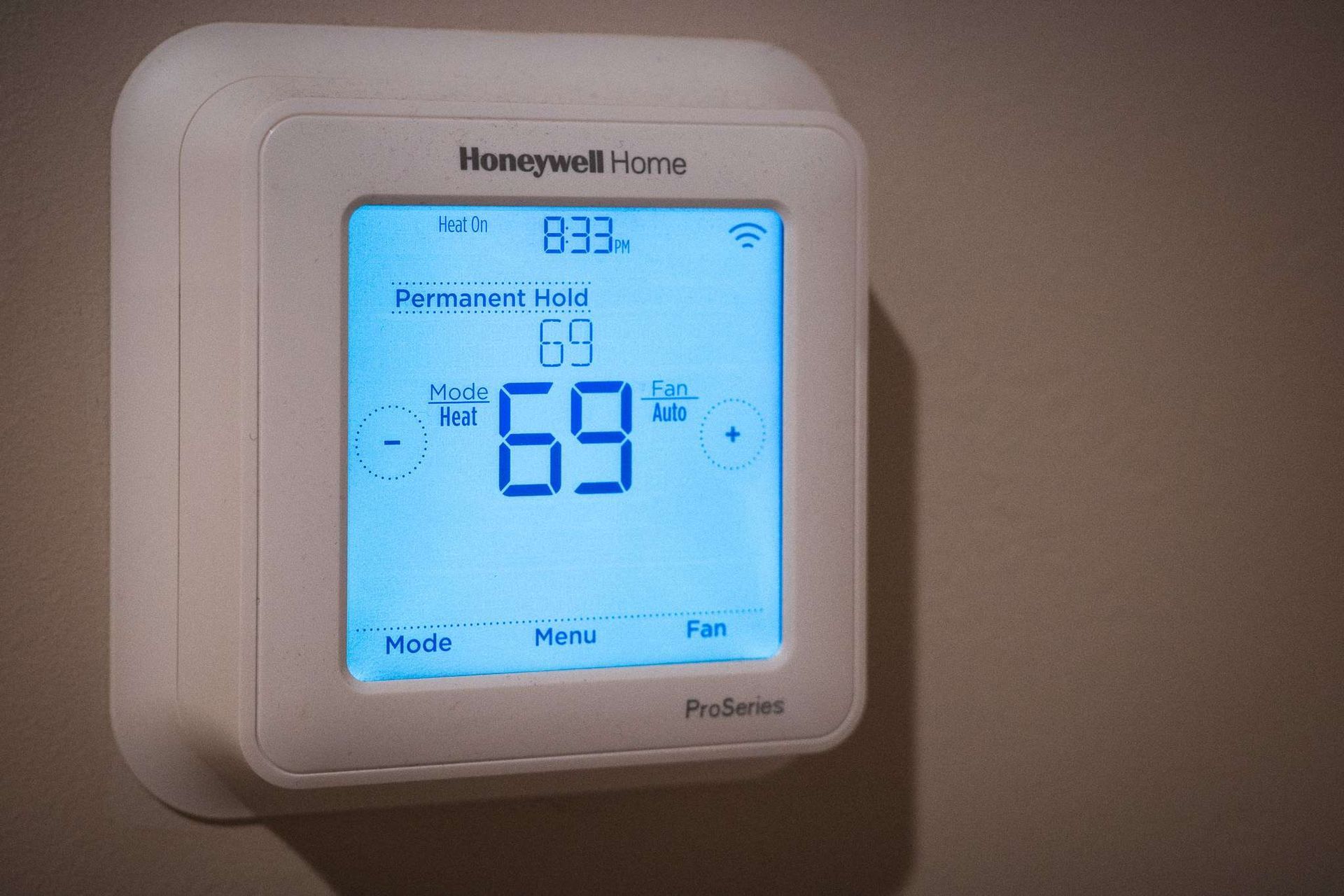 White Honeywell thermostat on a wall displaying temperature of 69°F and other settings.