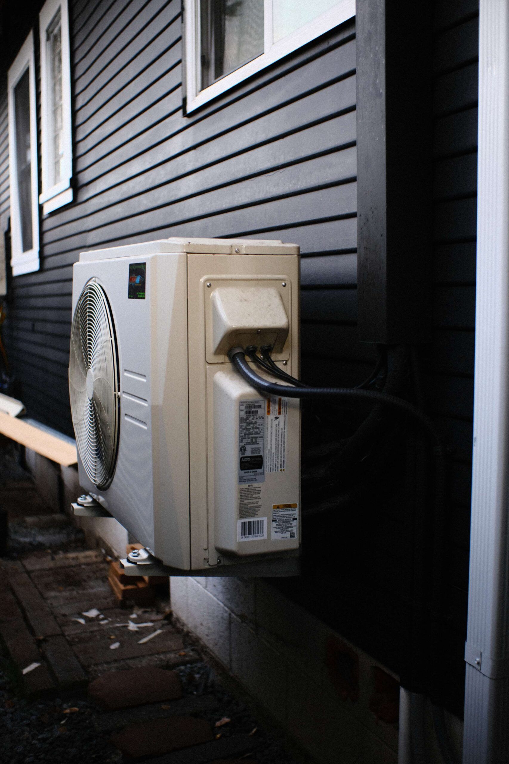 Cream-colored AC unit mounted on a black wall outside a building, with wires connected.