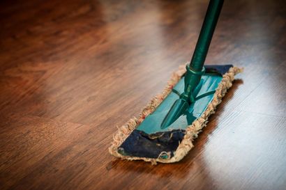 Green mop head on a wooden floor with visible dust and dirt.