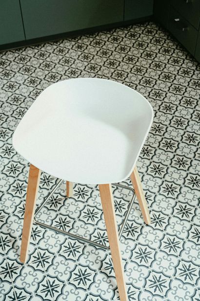 White chair with wooden legs on patterned tile floor in a corner room