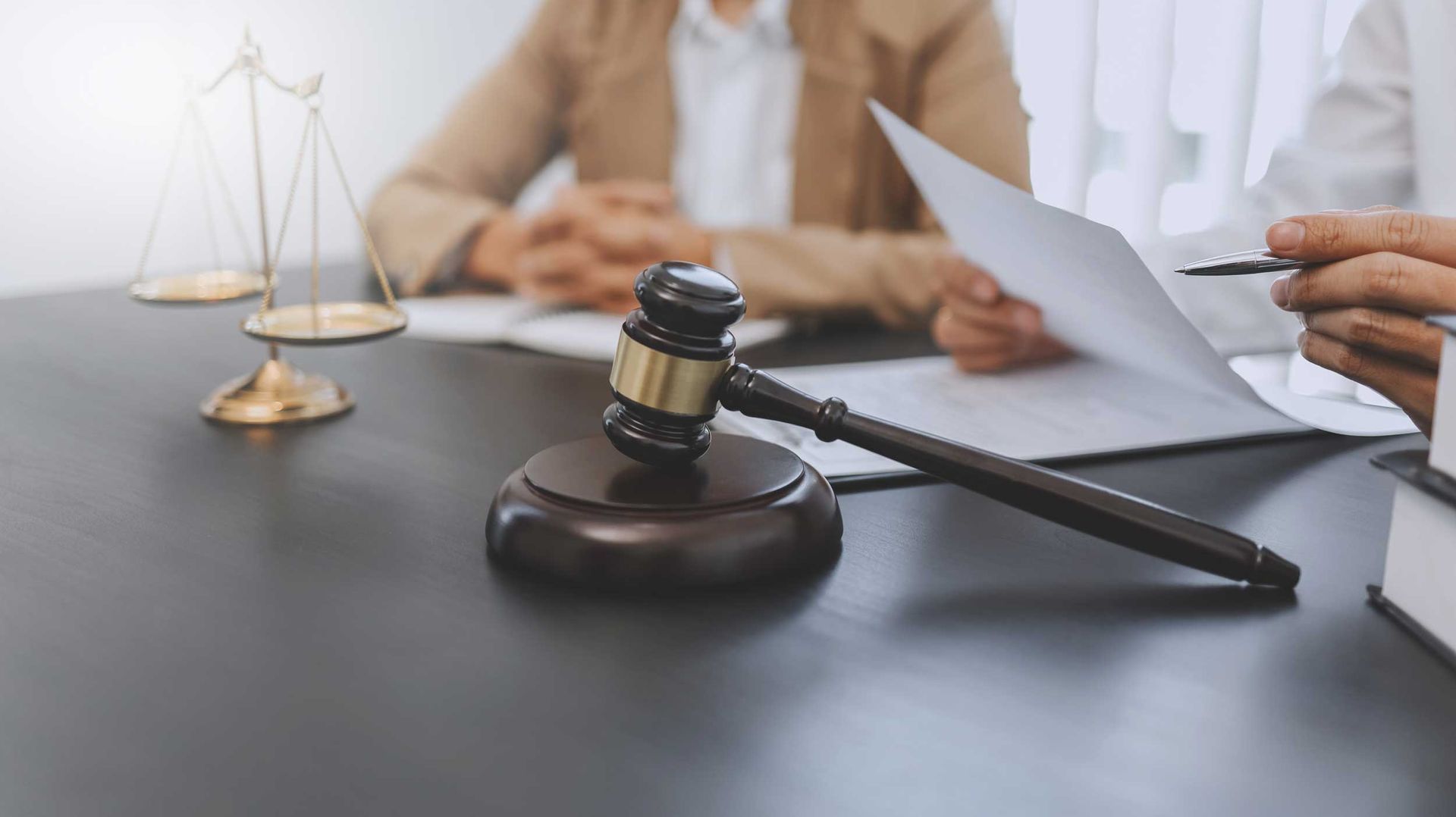 Gavel and legal documents on a desk as two people review papers in a law office setting.