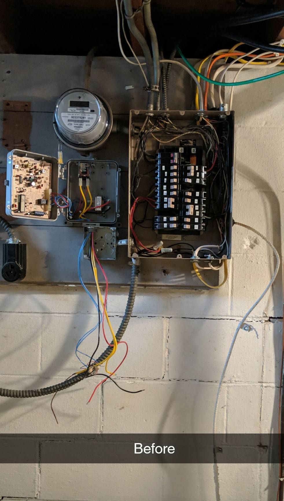 Open electrical panel with meter and exposed wiring on a wall, labeled “Before”