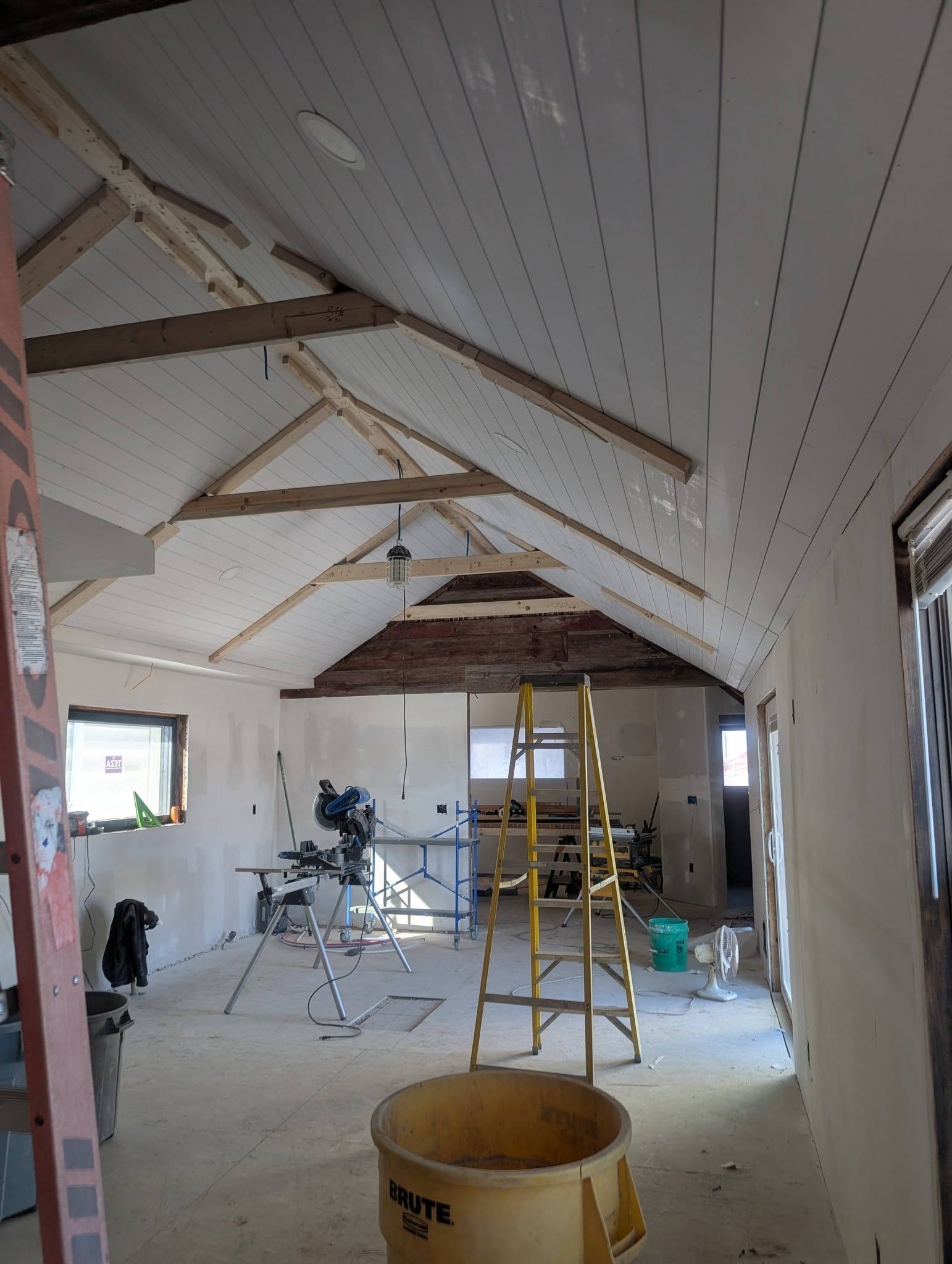 Renovation site with exposed beams, scaffolding, ladder, and tools in a long attic room
