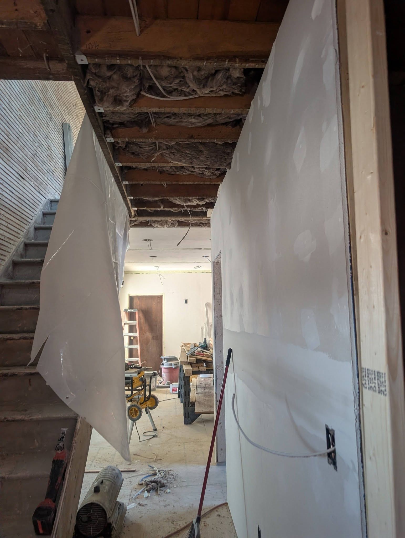 Narrow hallway under renovation with drywall, exposed ceiling beams, and construction materials scattered ahead