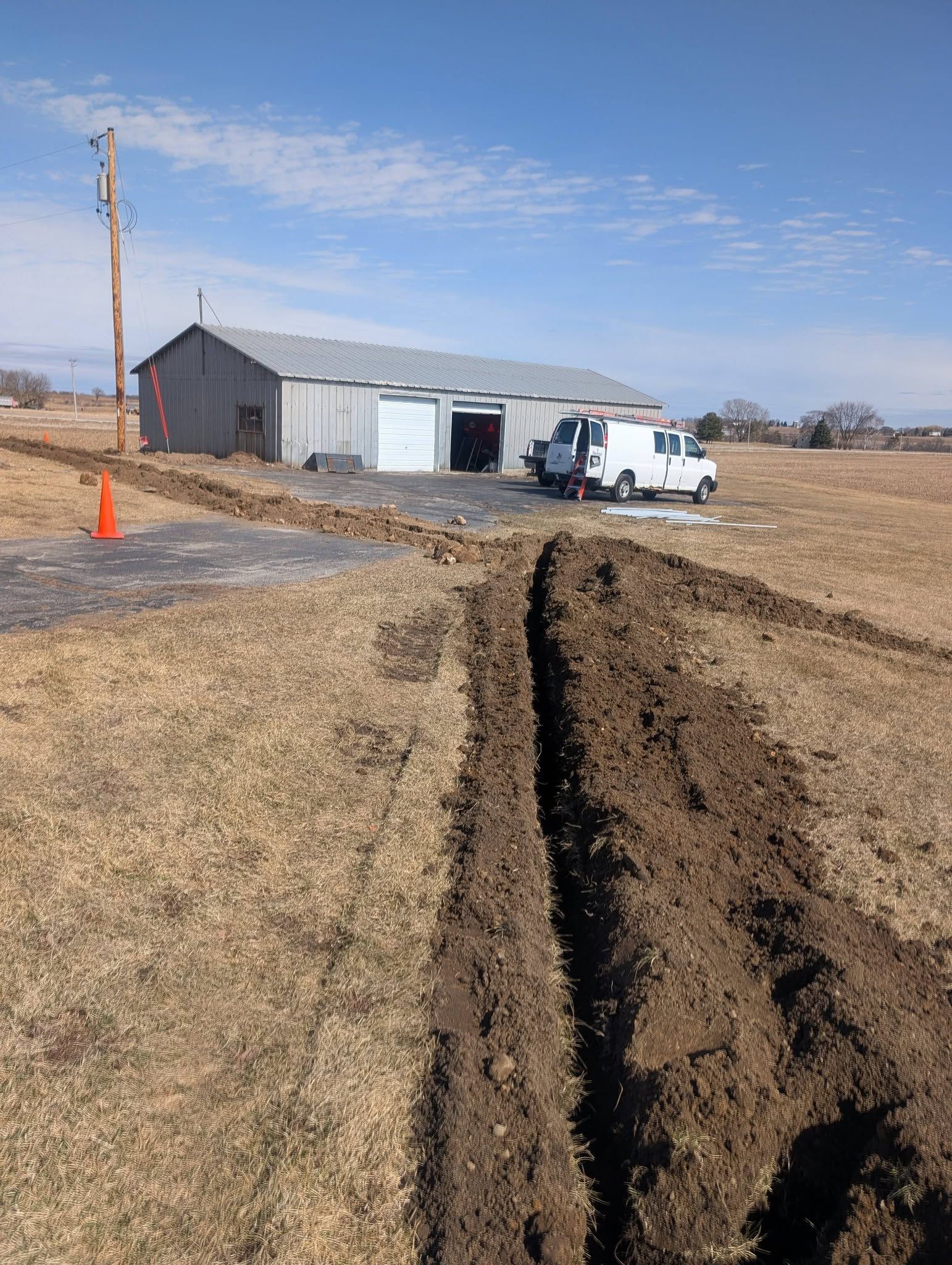 Rural driveway with deep tire ruts leading to a small garage and white van on a dry, grassy lot.