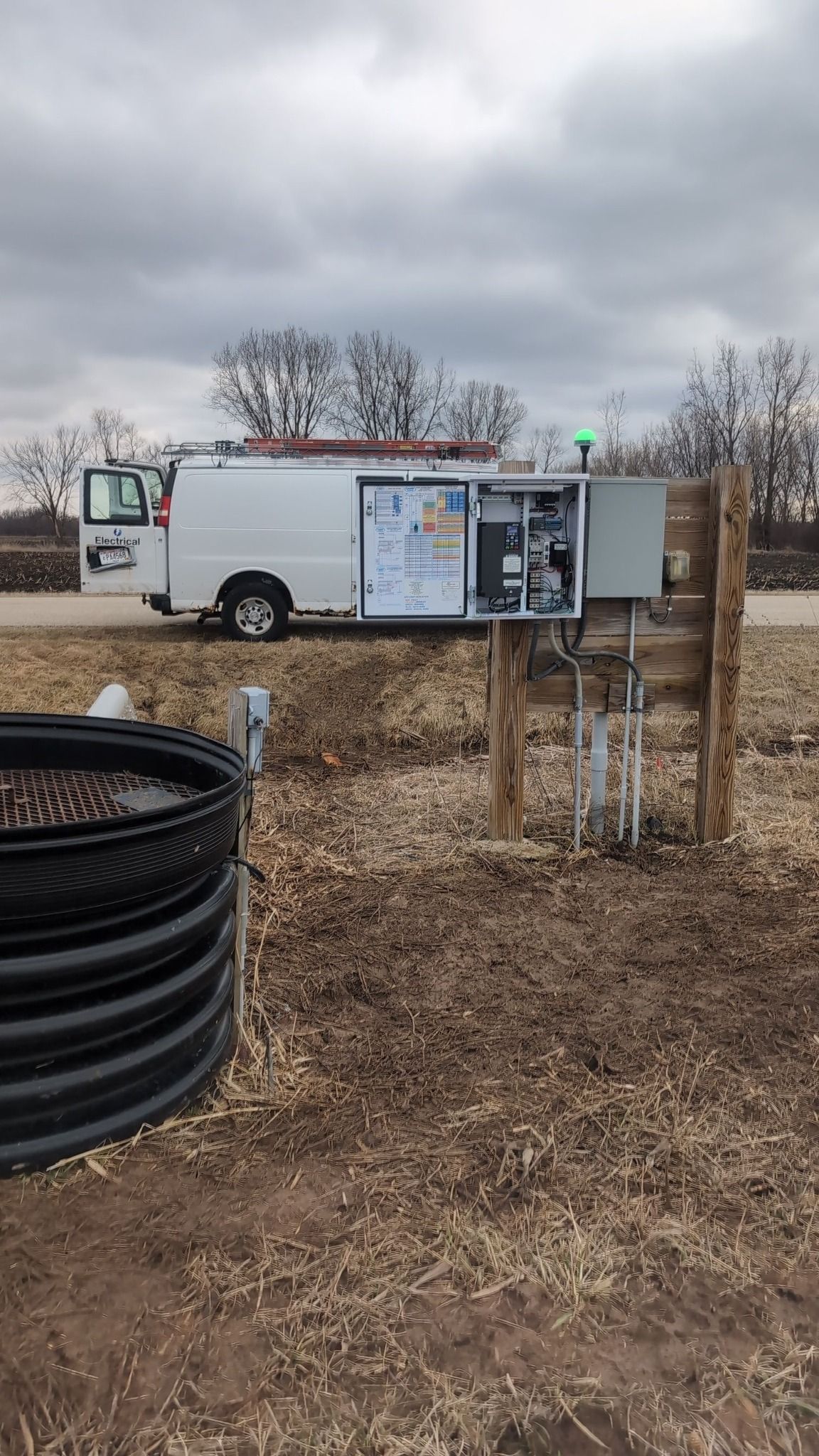 White utility trailer with attached panels in a field under cloudy sky, beside a black coiled hose.