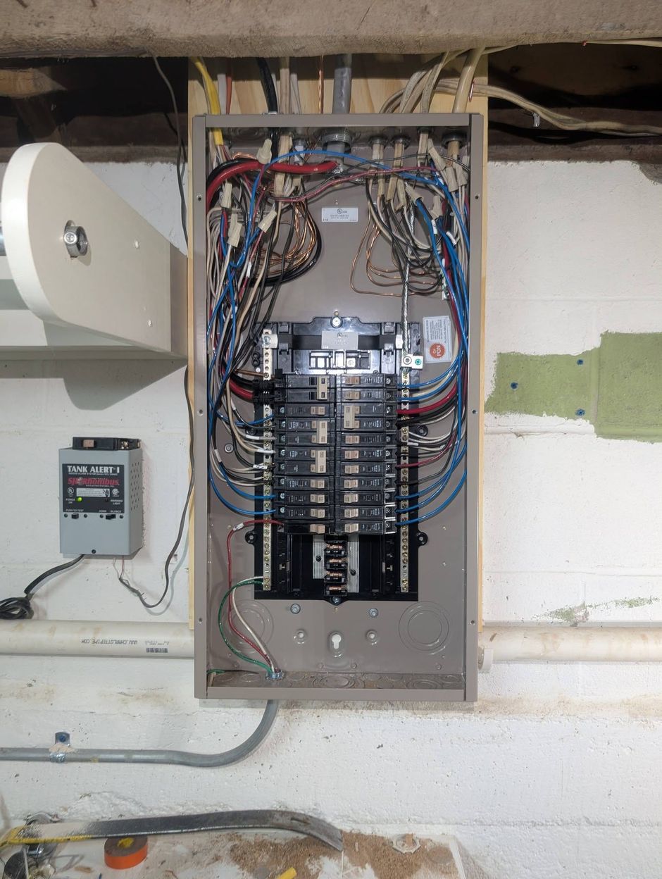 Open electrical panel with multiple circuit breakers and wiring in a basement wall.
