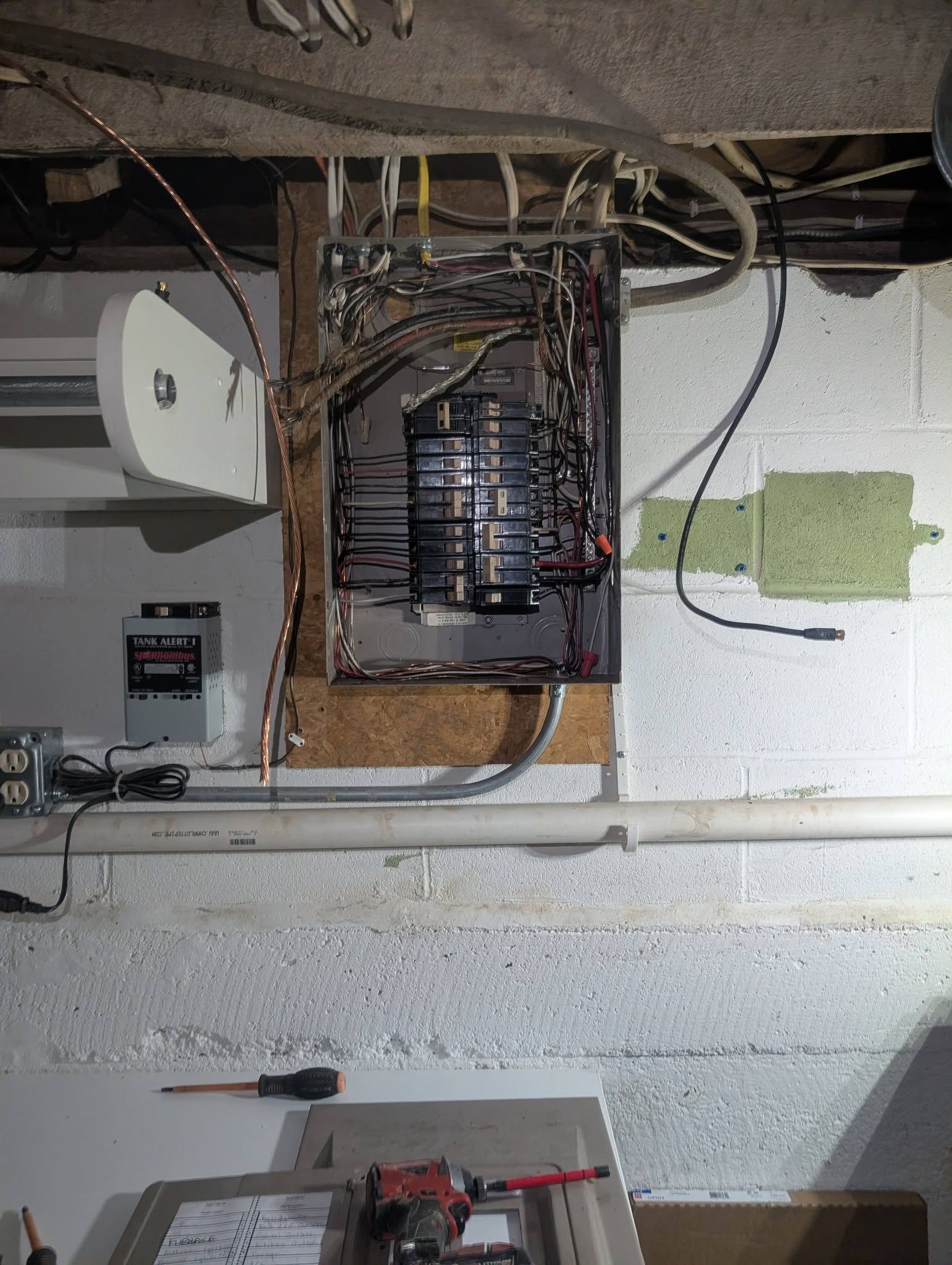 Open electrical panel with exposed wiring and breakers on a basement wall.