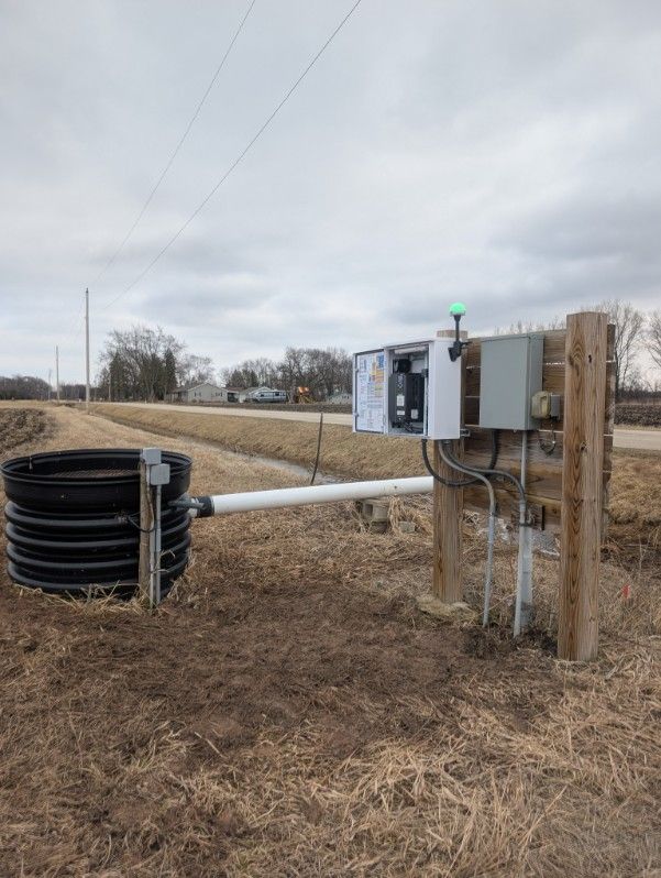 Rural utility equipment beside a black cylindrical tank on a cloudy roadside field
