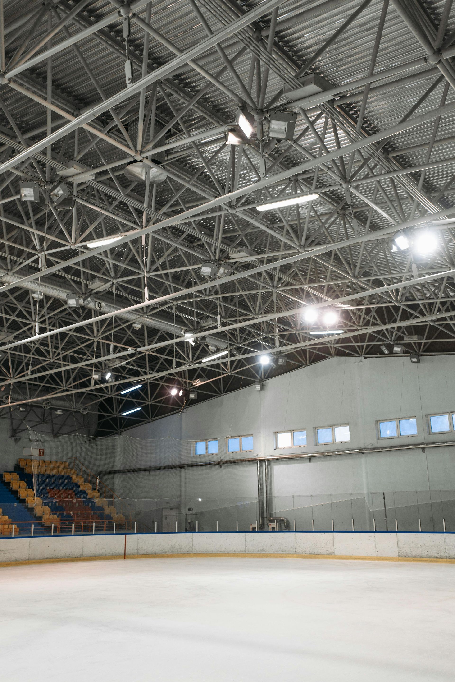 Indoor ice rink with empty ice, bright lights, and steel truss ceiling