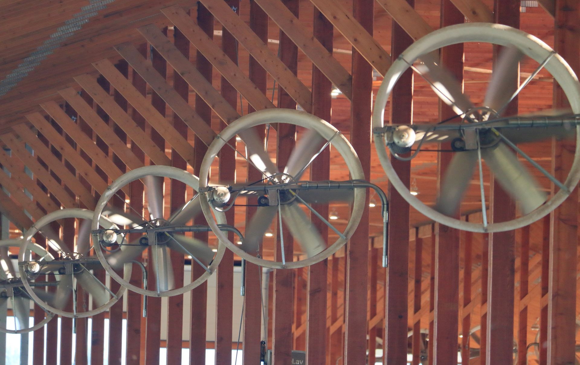 Row of metal pulley wheels mounted under a wooden roof with red beams and brick walls