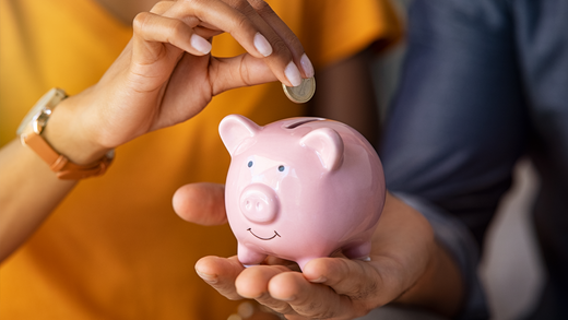 a woman is putting a coin into a pink piggy bank .