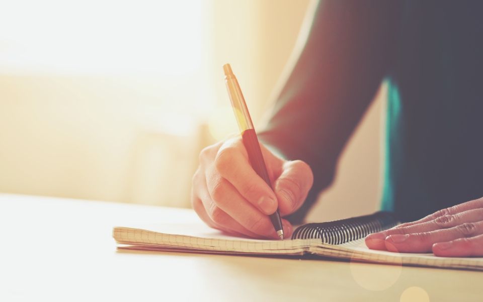 hands with pen writing on notebook