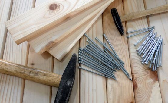 A hammer , nails , and pieces of wood on a wooden table.