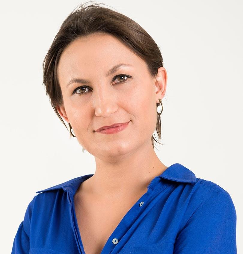 A woman wearing a blue shirt and earrings smiles for the camera