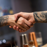 A man with a tattoo on his arm shakes hands with another man