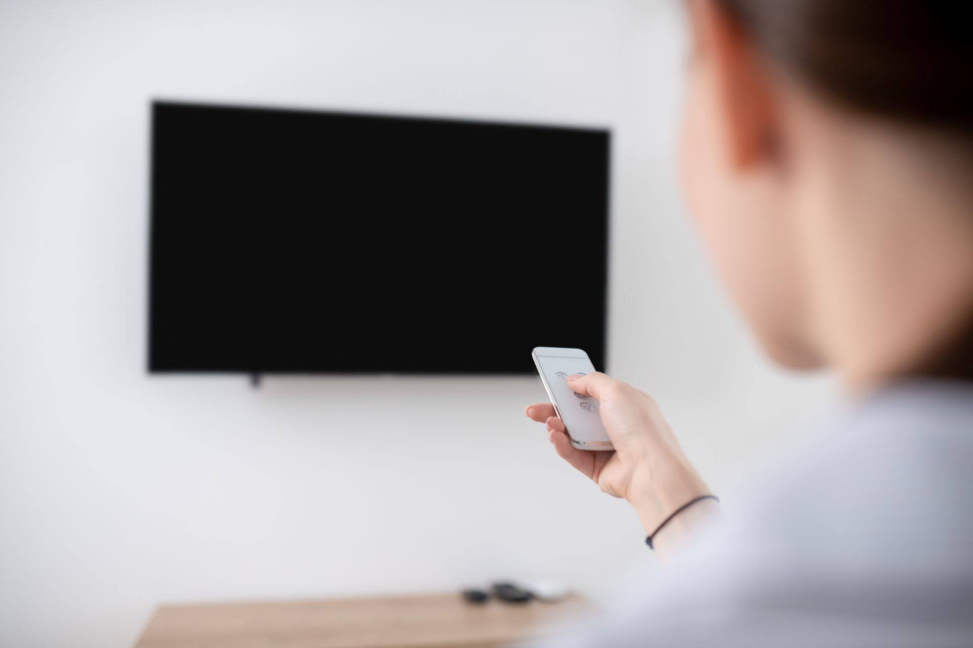 Person holding a remote control pointing at a black screen television mounted on a white wall. — Audiomation in Wingham, NSW