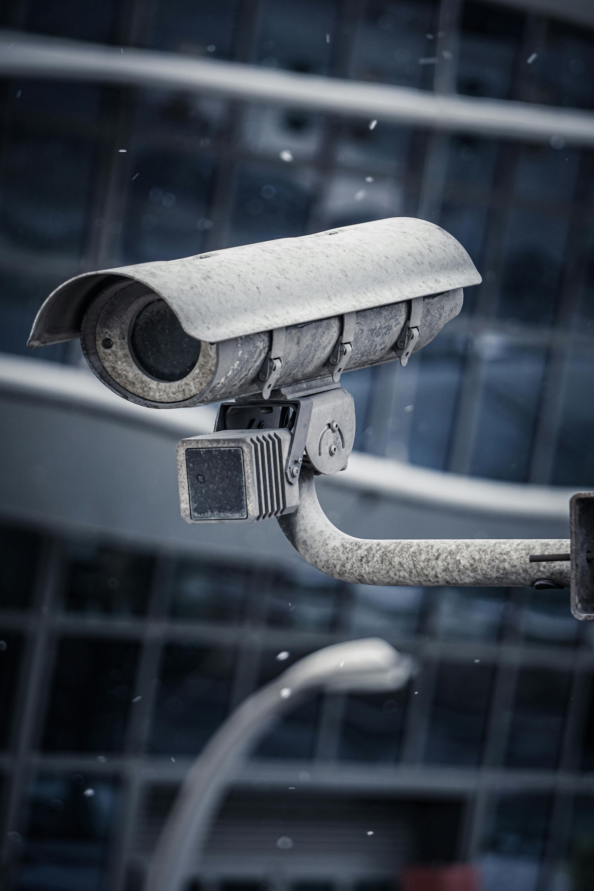 Security camera mounted on a pole, snow falling. Building background.