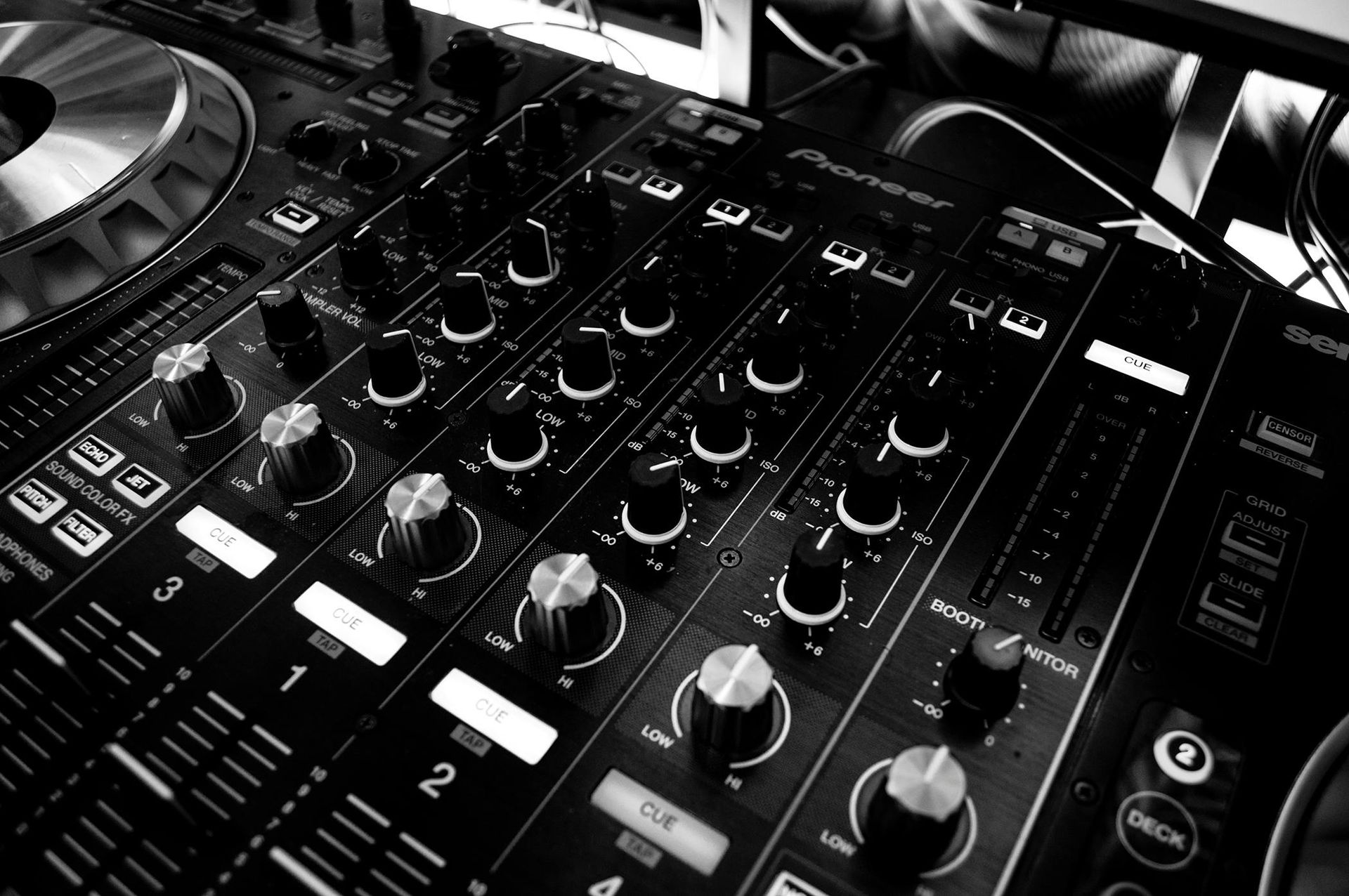 Black and white close-up of a Pioneer DJ mixer with knobs, faders, and a turntable, ready to play music.