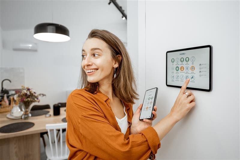 Woman smiling, using smart home control panel on tablet and phone in a modern kitchen.
