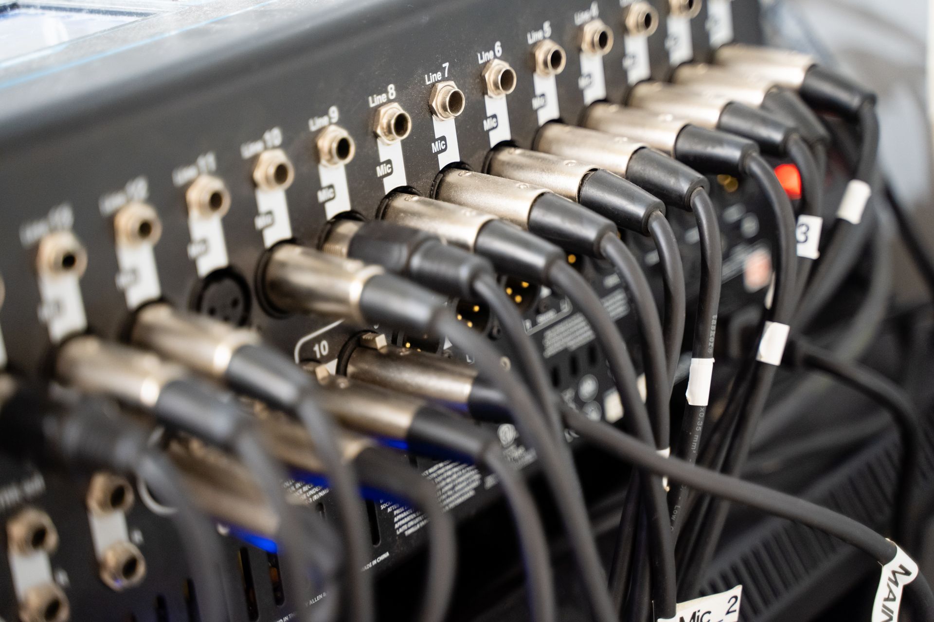 Close-up of a black audio mixer with numerous cables plugged in.