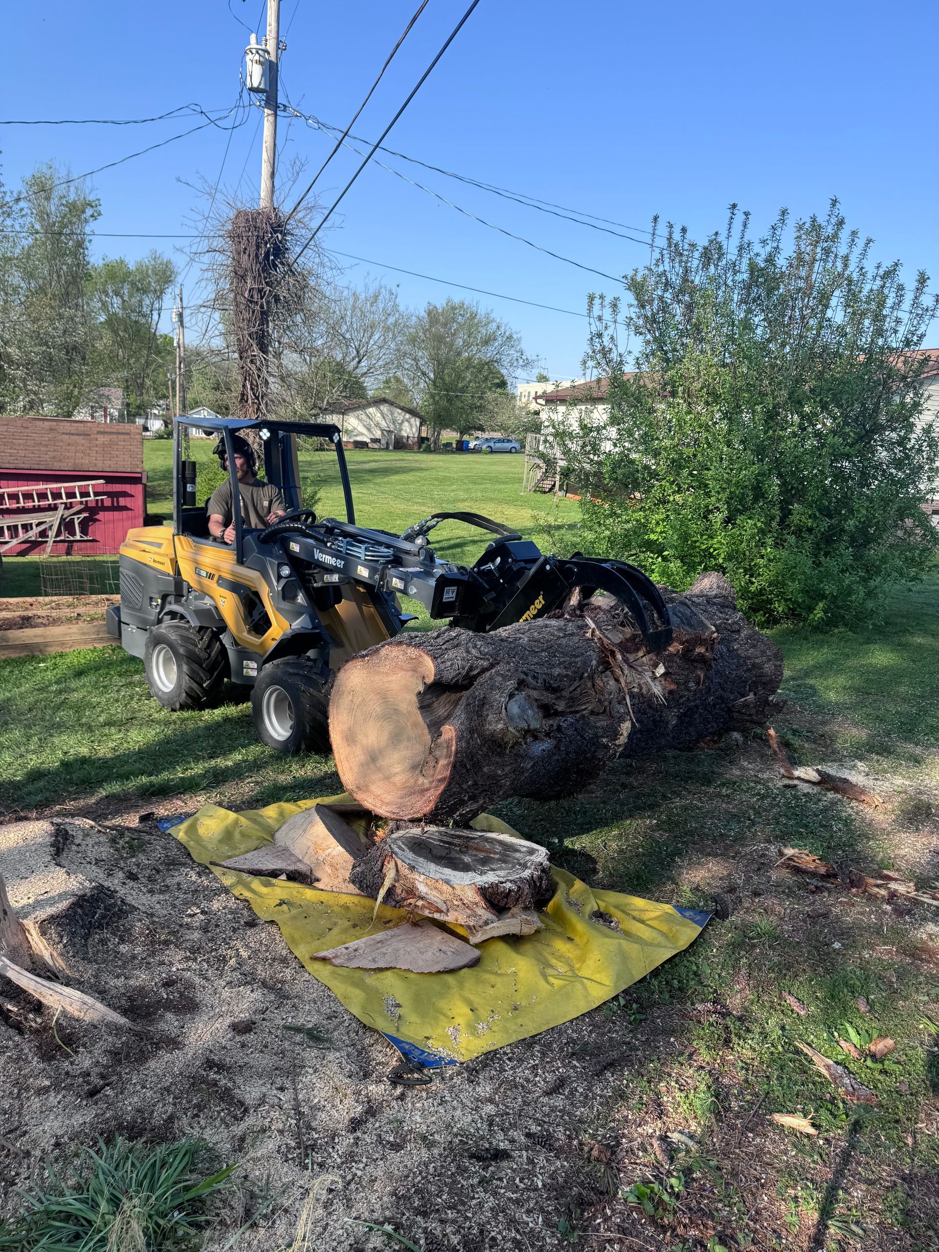 A tractor is cutting a tree stump in a yard.