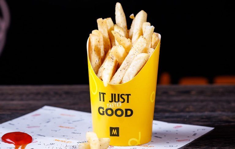 A yellow cup filled with french fries that says it just tastes good