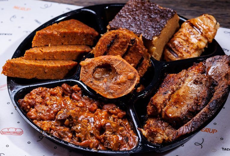 A black tray filled with a variety of food including meat and beans