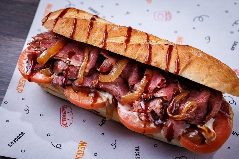 A sandwich with meat , tomatoes and onions is on a piece of paper.