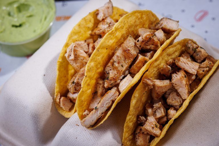 Three tacos are sitting on a napkin next to a bowl of guacamole.
