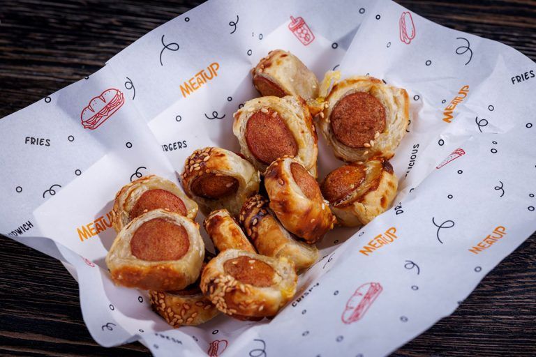 A basket of hot dogs wrapped in puff pastry on a piece of paper.