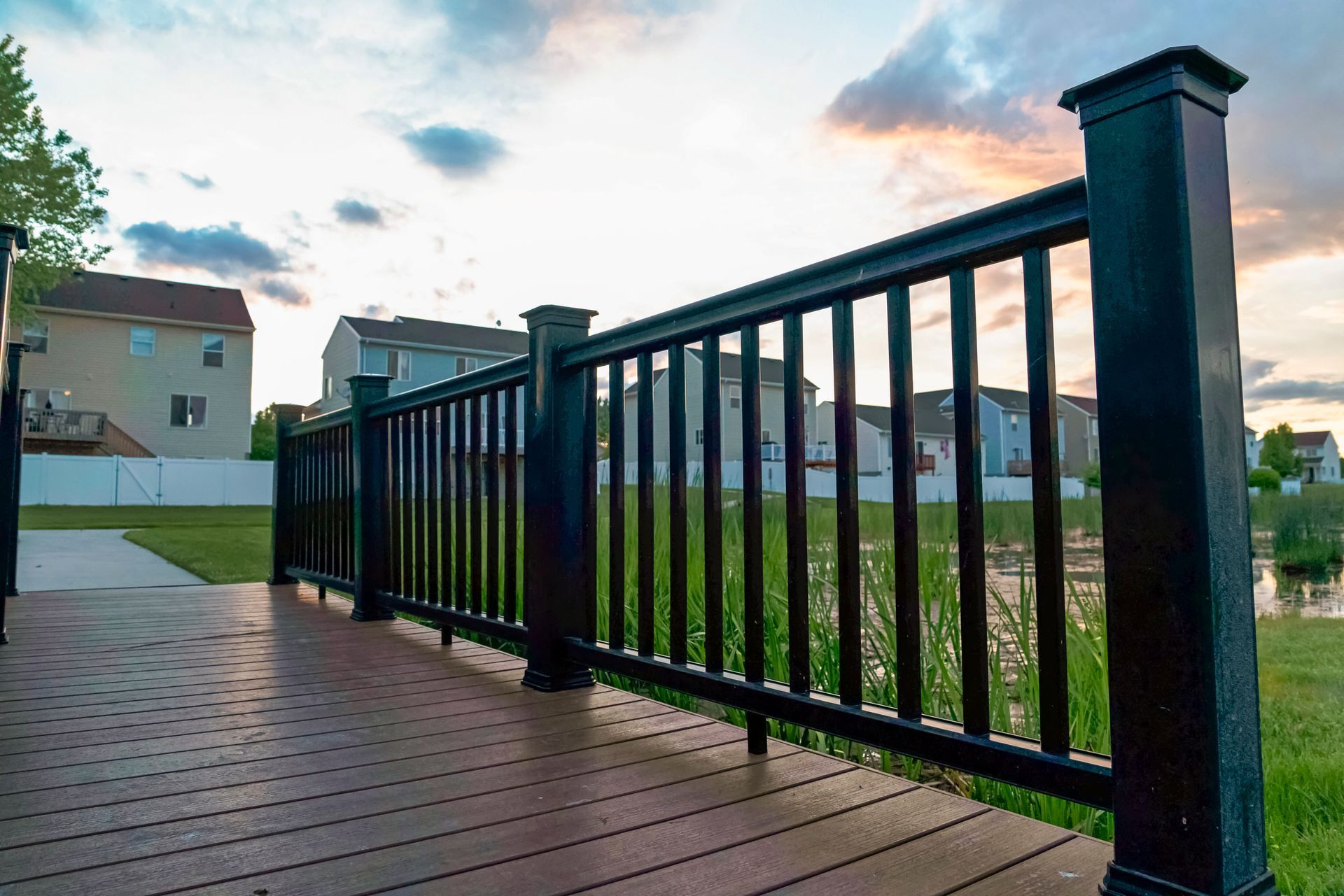 A wooden deck with a black railing and a house in the background.