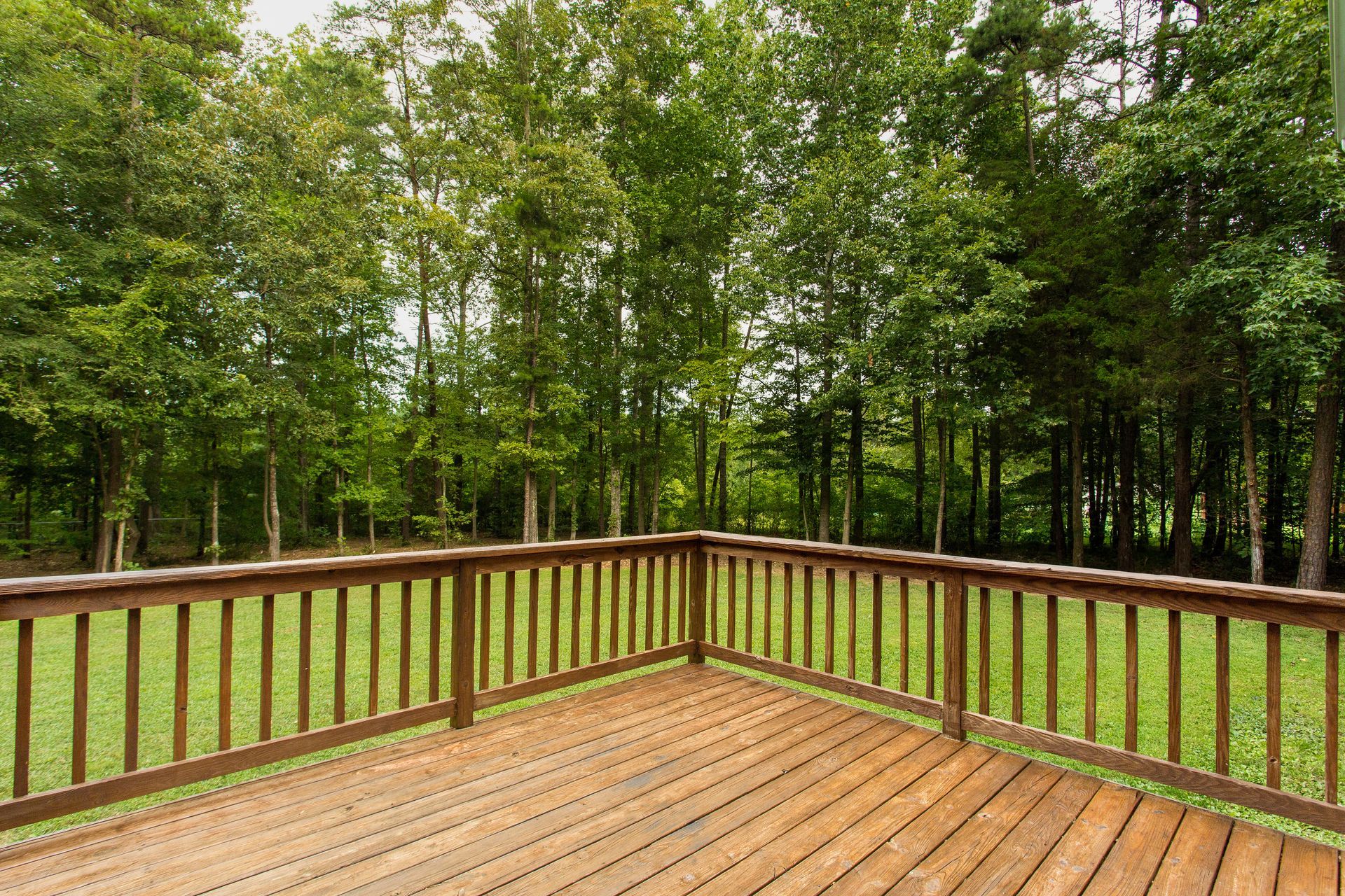An empty wooden deck with a wooden railing surrounded by trees.