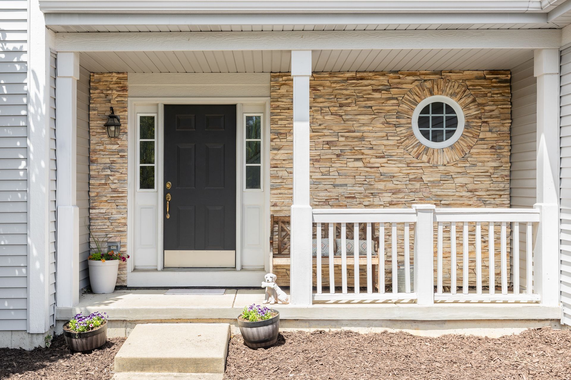 The front porch railing of a house with a black door and a stone wall.