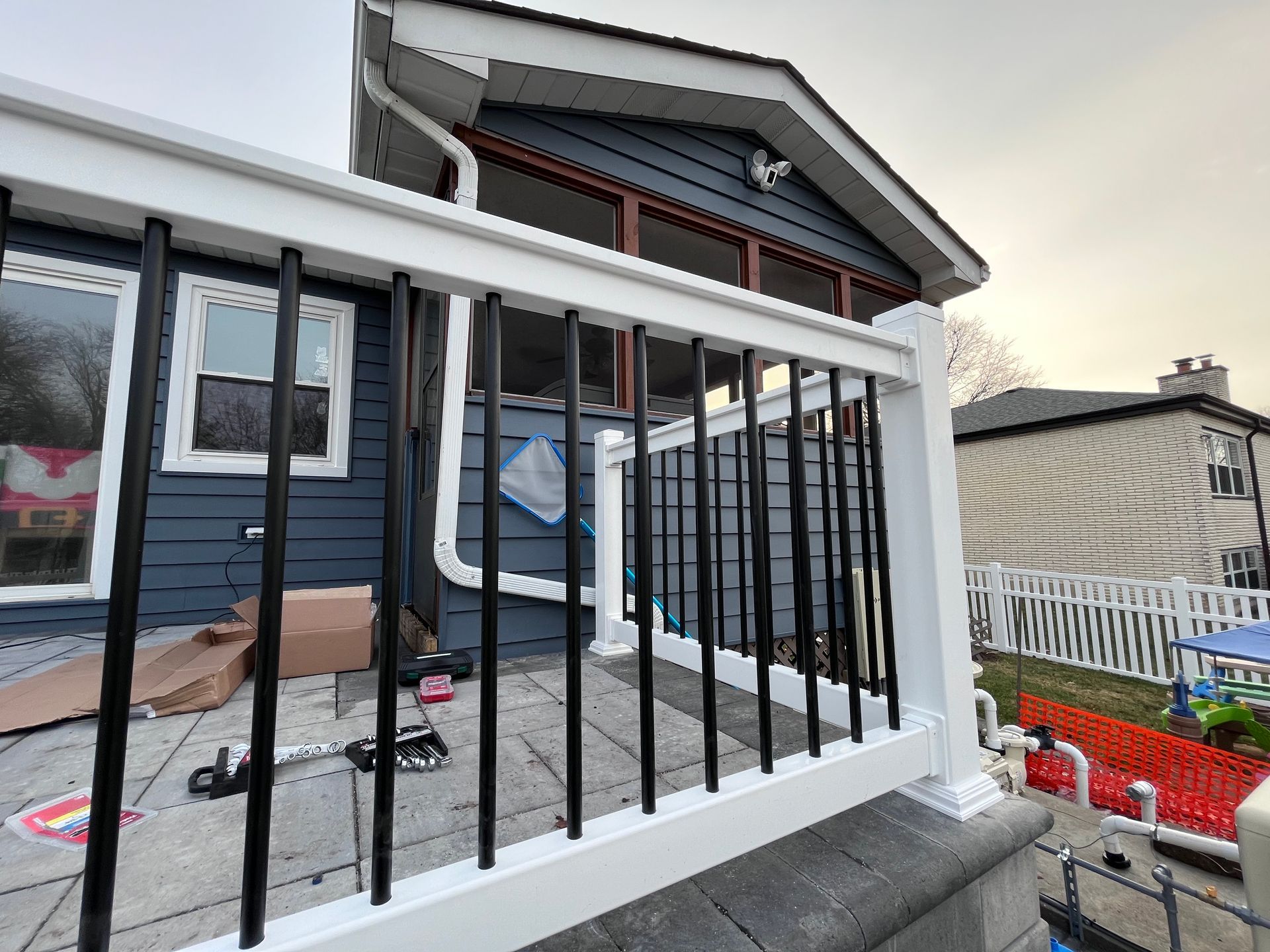 A white railing with black bars is sitting in front of a blue house.