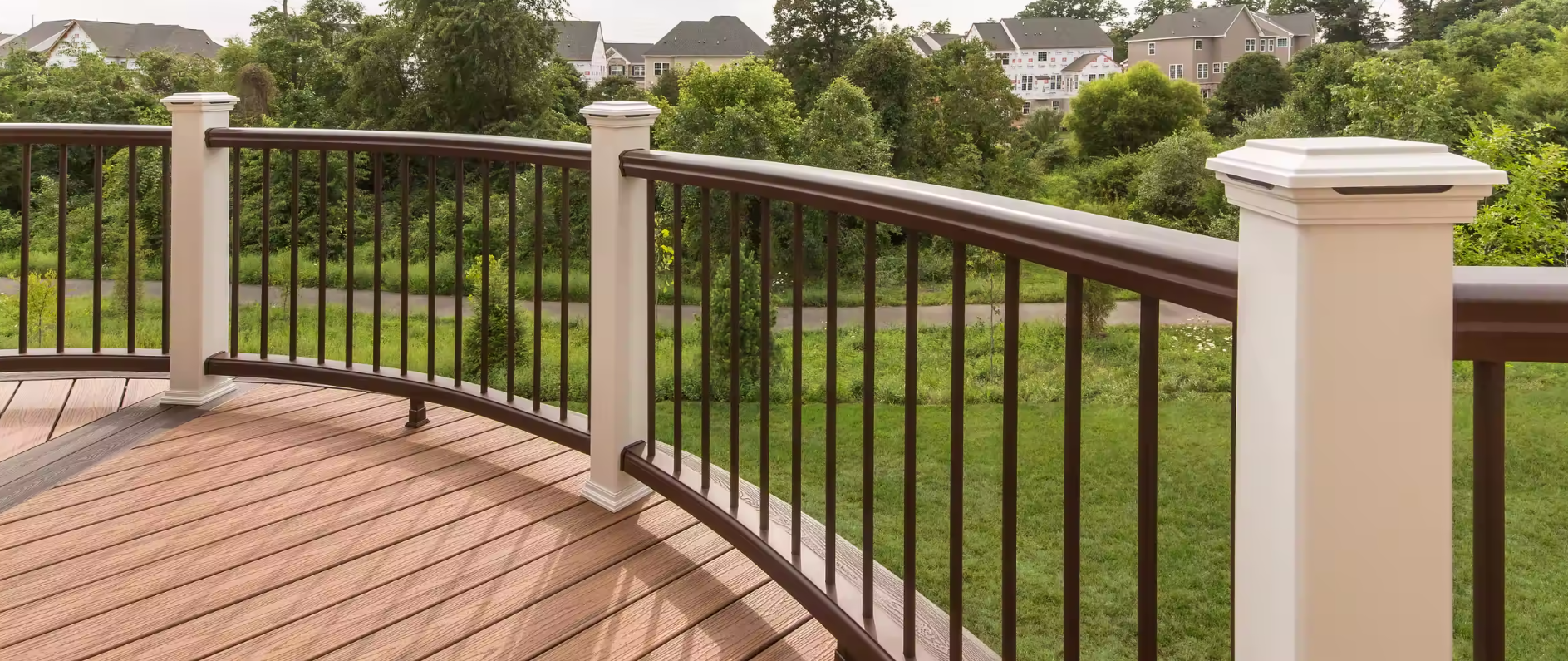 A composite deck with a curved trex railing and a view of a park.